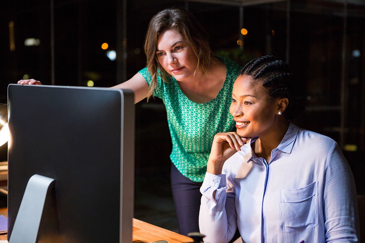 Two women collaborating on SEO-friendly web development project on a computer.