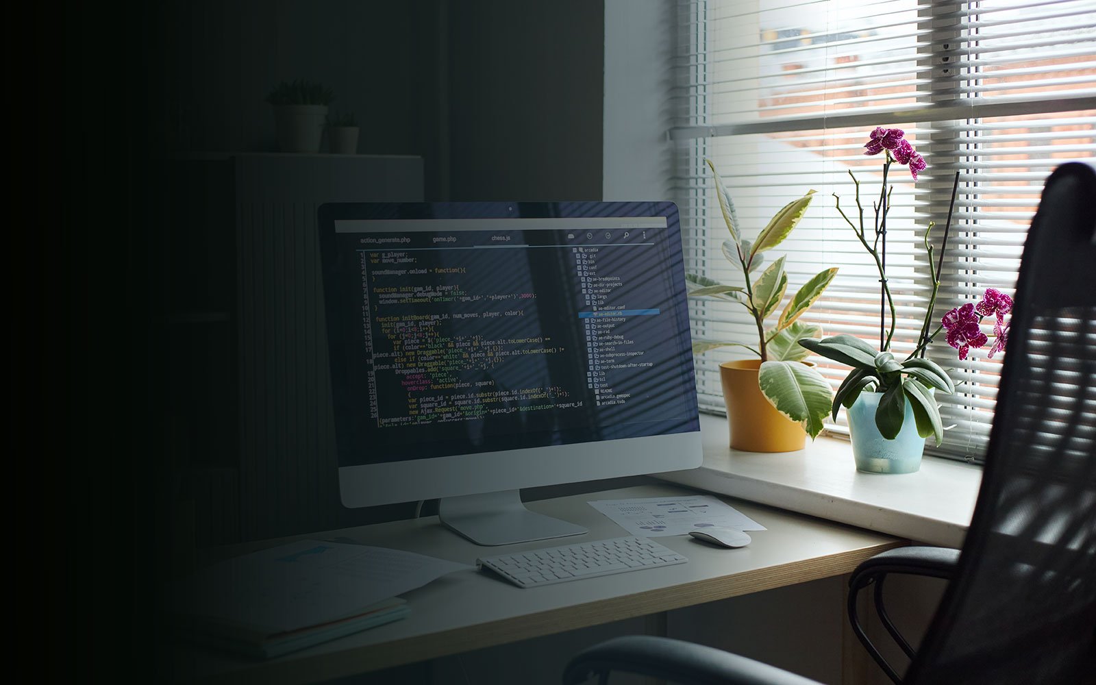 Computer screen displaying coding interface, desk, plants, and window blinds