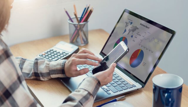 Hands on laptop and phone analyzing business report for SEO friendly web development.
