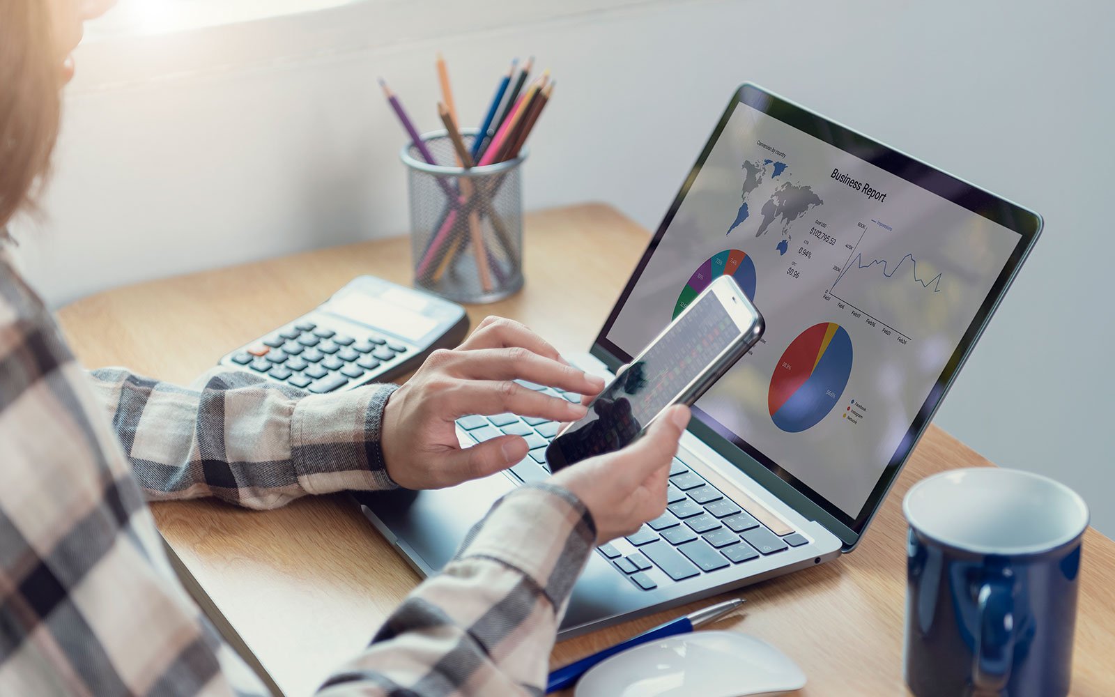 Hands on laptop and phone analyzing business report for SEO friendly web development.